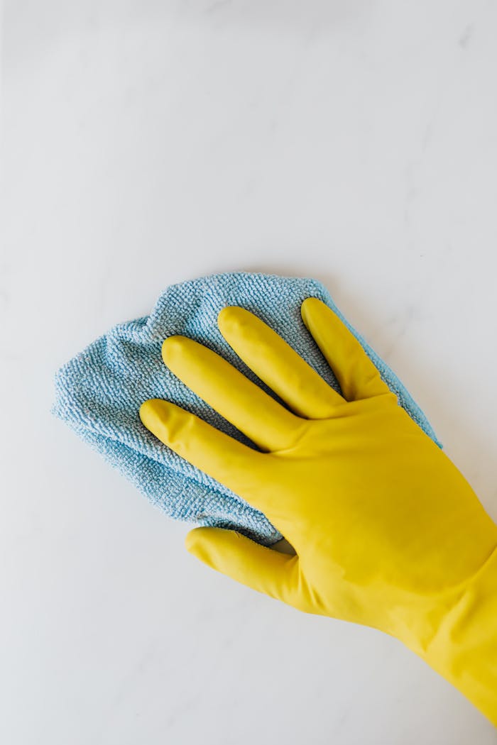 Crop unrecognizable person in yellow gloves cleaning white surface